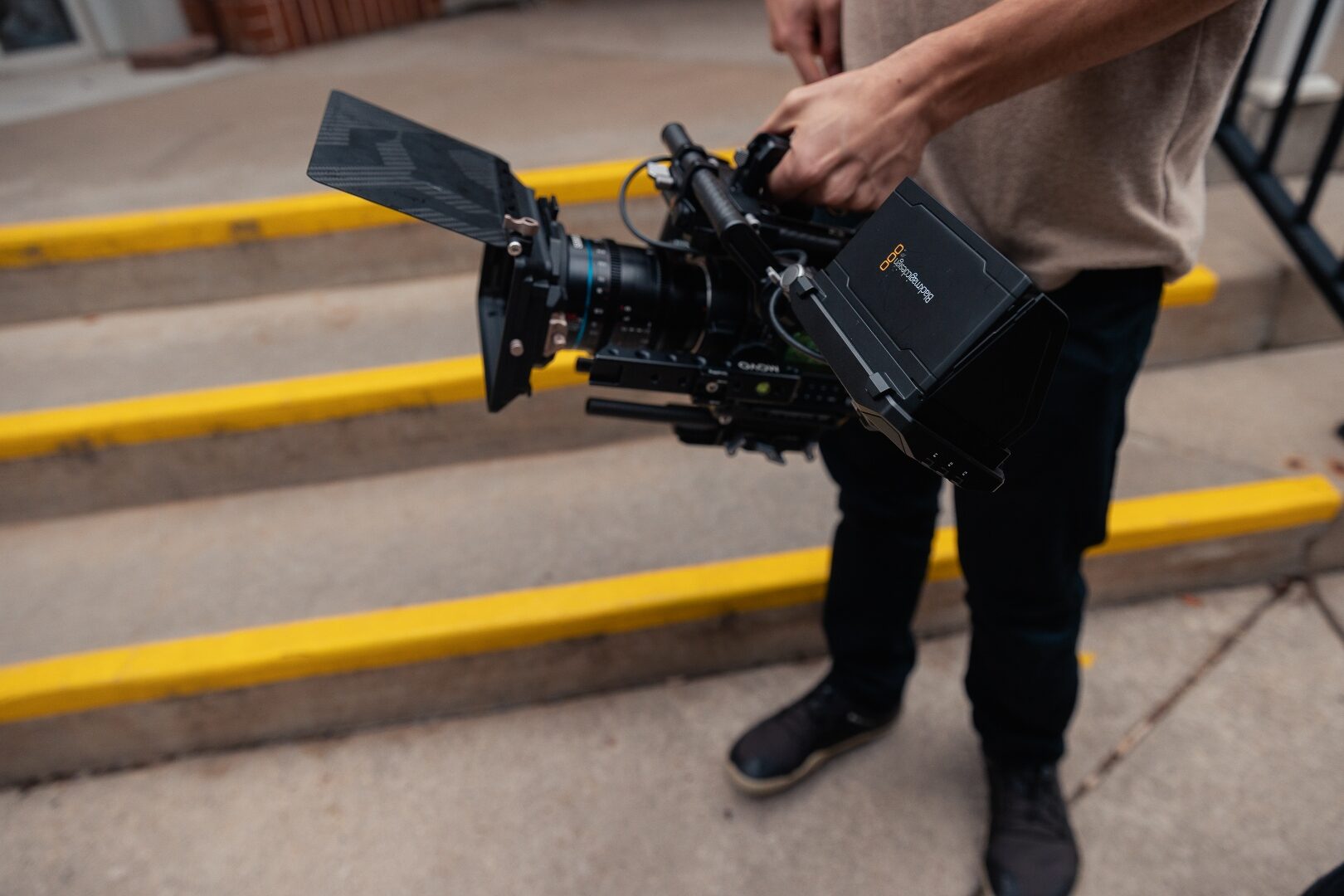 Hands holding a Blackmagic cinema camera over yellow painted curb stops.