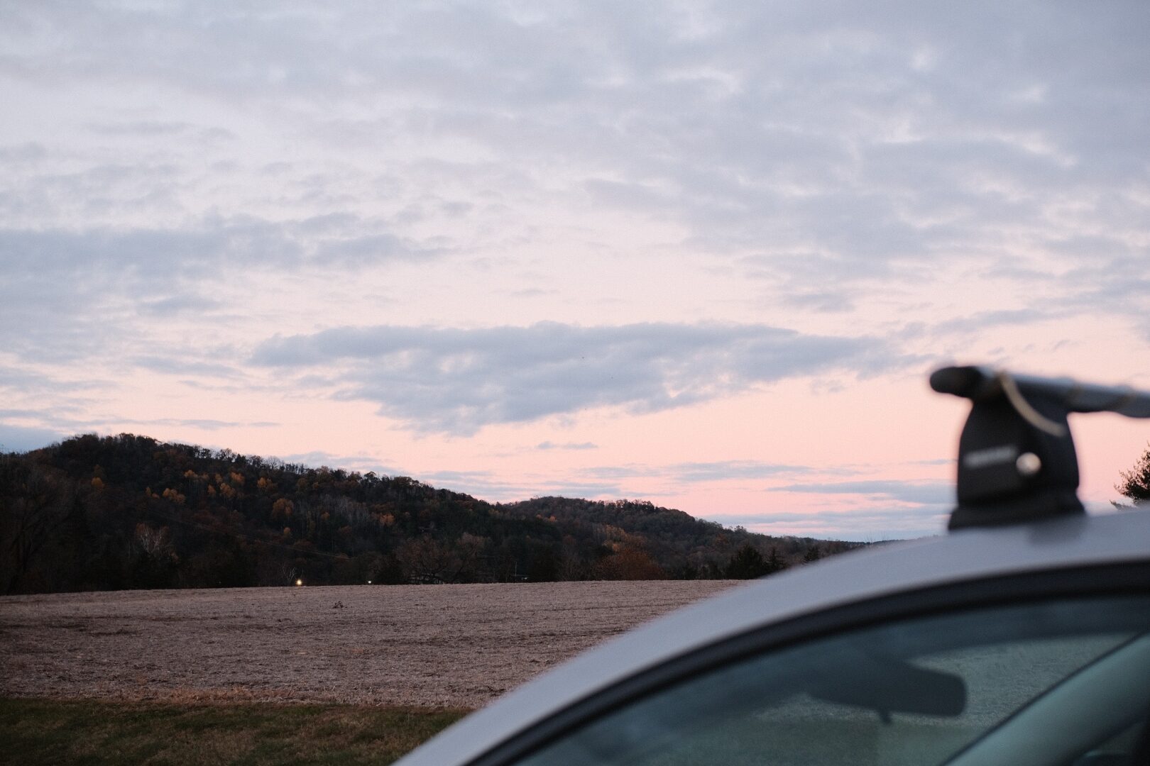 A soft pink dusk over the Wisconsin bluffs, seen from the side of a parked car.